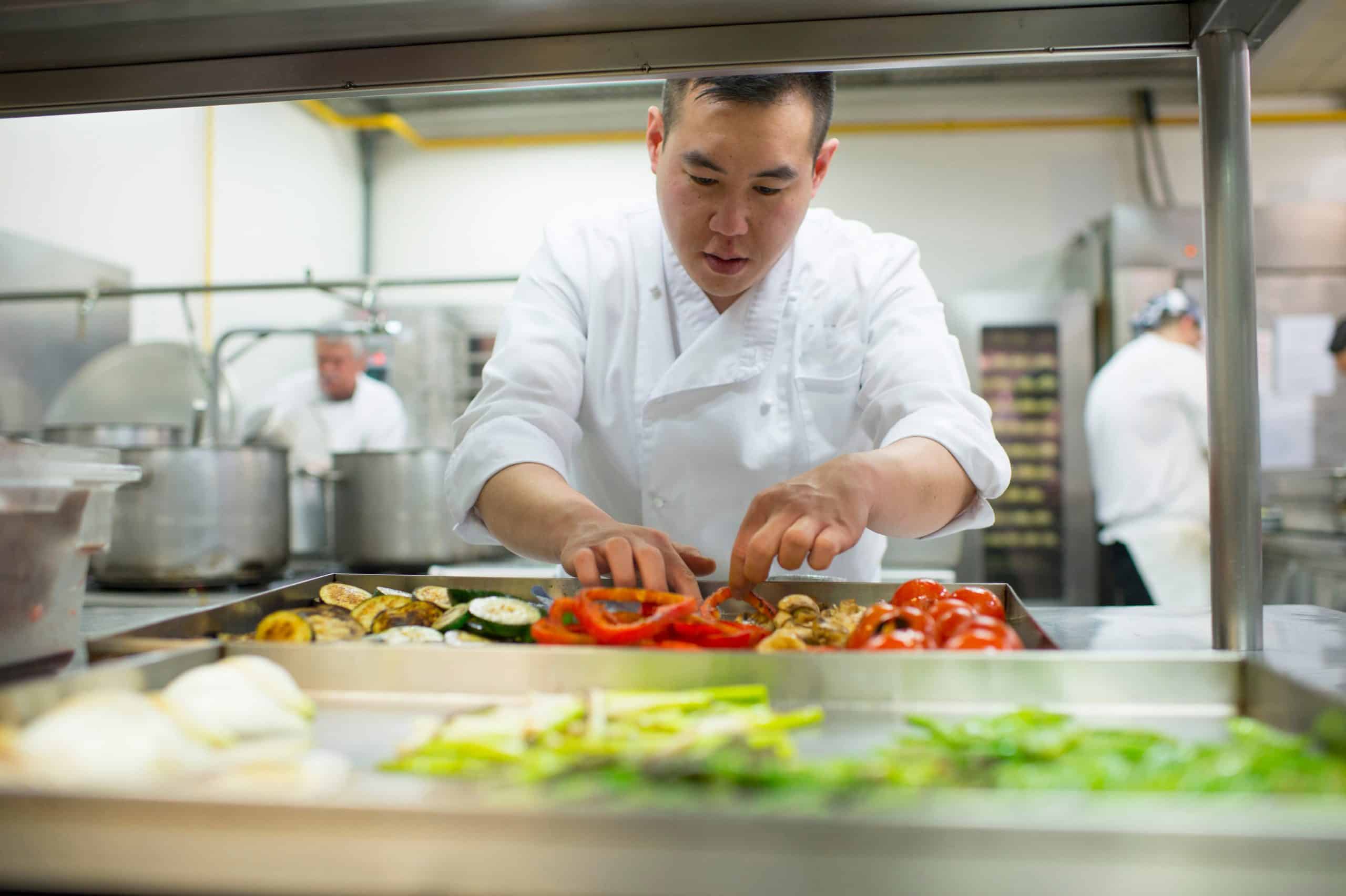 Un cuisinier en train de manipuler des aliments dans des bacs inox rangés sur des étagères de rangements alimentaires